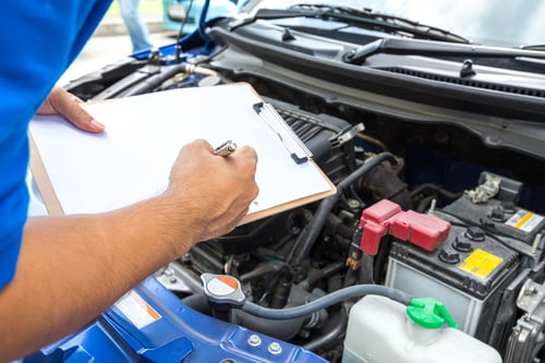 person writing on clipboard over car engine